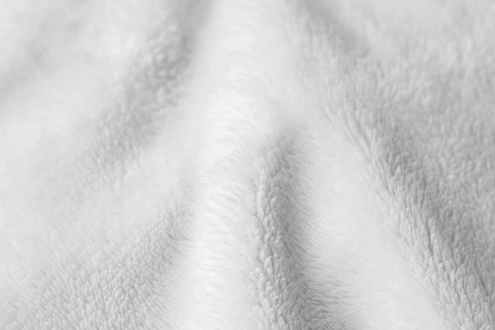 Close detail of a soft white cut-pile textile with folds catching raking light.